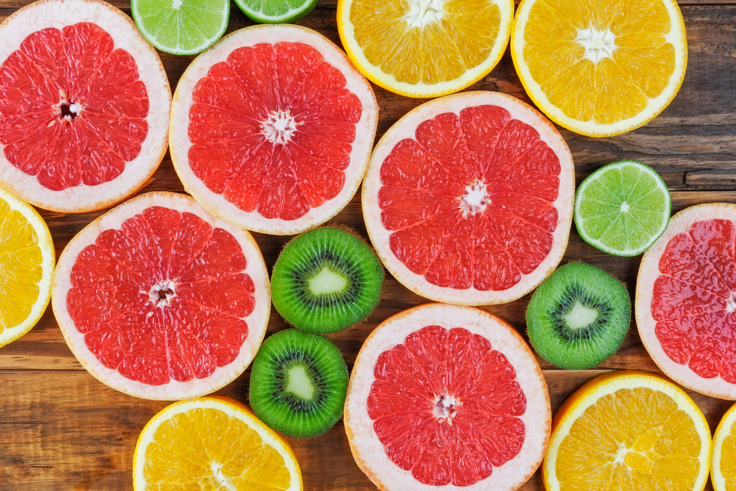 Slices of red grapefruit, lime, orange, and kiwi arranged on rustic wooden table closeup. Top view.
